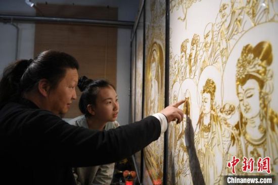 该画取材《灵山说法图》,内容涉及人物95个、瑞兽2只,掐丝勾勒出的人物神态、服饰、动作等栩栩如生。图为李海明正在给女儿李婕讲解其中的手艺精髓。