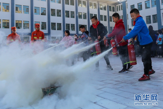 在甘肃省森林消防总队张掖市支队指战员指导下,甘泉街小学学生学习使用干粉灭火器。新华网发 (张小军 摄)
