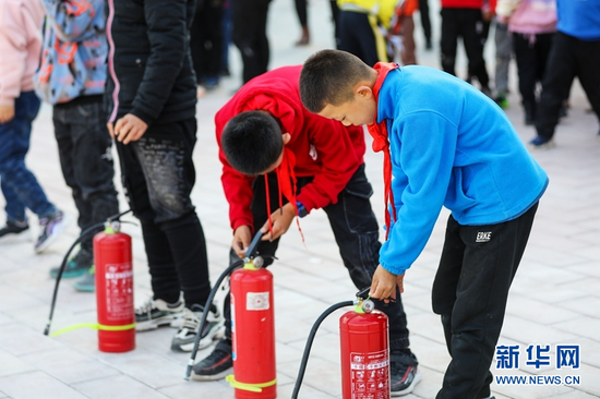 在甘肃省森林消防总队张掖市支队指战员指导下,甘泉街小学学生学习使用干粉灭火器。新华网发 (尤国功 摄)
