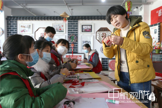 孩子们跟老师学习剪纸。