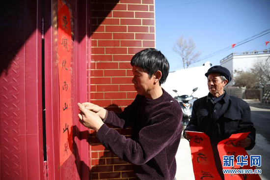 2月11日,元古堆村村民韩喜红(左)和父亲在家门口贴春联。新华社记者 马希平 摄