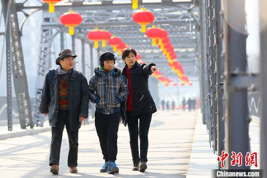 2021年春节期间,台湾商人杜书亿一家三口走过挂满火红灯笼的兰州中山铁桥。 中新社记者 高展 摄