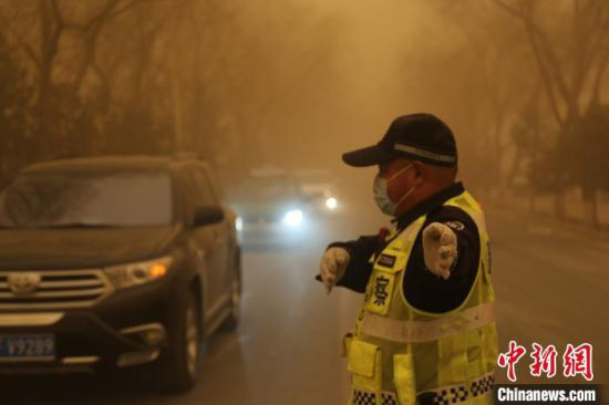 图为3月15日,甘肃多地遭遇沙尘天气,一名交警戴口罩执勤。 俞治海 摄