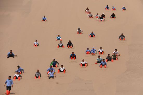 2021年6月13日,市民游客在甘肃省敦煌市鸣沙山月牙泉景区滑沙。
