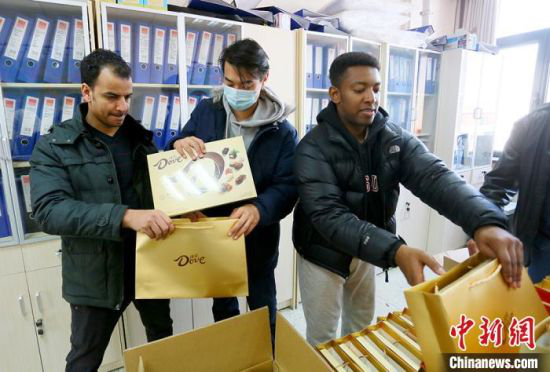 该校留学生马弈、阿布、王山木(从左至右)协助老师为留学生发放“春节大礼包”。 高展 摄