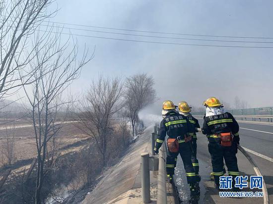 2月21日,海石湾往兰州方向高速公路道旁树木着火,消防员正在灭火。