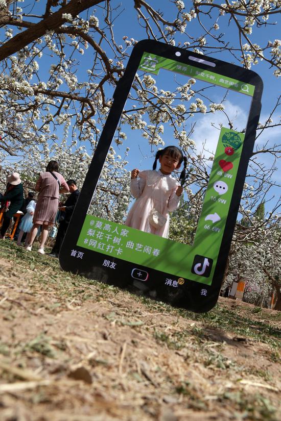 2021年4月17日,小朋友在甘肃省敦煌市莫高镇泾桥村梨园中拍照。