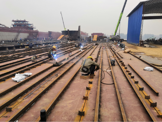 造船工人正在用电焊机焊铺在地面上的钢板，紧锣密鼓地进行着12艘纯LNG燃料动力船建造工作。