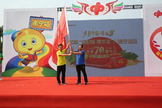 南宁市福彩中心负责人将健步走旗帜交回到广西福彩中心副主任梁卫手中