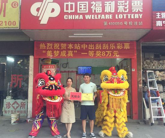 图为:南宁福彩工作人员为中奖投注站业主(右)颁发中奖牌匾及奖励金