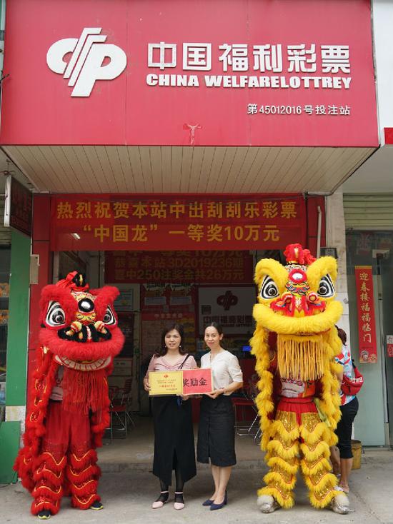 图为南宁市福彩中心工作人员为中奖投注站业主(左)颁发牌匾与奖励金