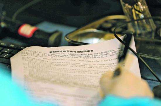 对接种人员进行健康询问后,医护人员在新冠肺炎疫苗接种知情同意书上签字。
