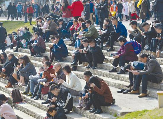24日,市民们坐在湿地公园的石阶上晒太阳。