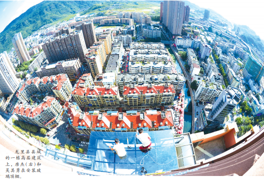 龙里县县城的一栋高层建筑上,唐杰(右)和吴其勇在安装玻璃顶棚。