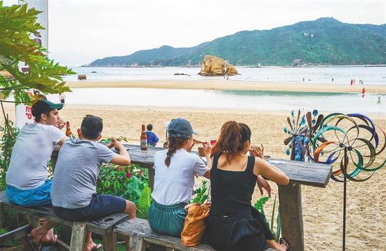 坐在海边喝着冷饮的游客，正享受三亚后海放松闲适的氛围。海南日报记者 武威 摄