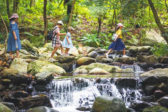  百花岭热带雨林文化旅游区，游客穿越溪流。本报记者 李天平 摄