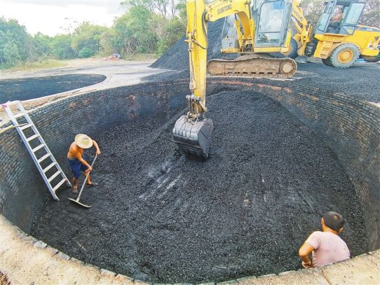 日前，在海口马禄村附近一椰壳露天烧炭黑加工点，烧炭灶内的工人在配合挖掘机挖炭。肖开刚 摄