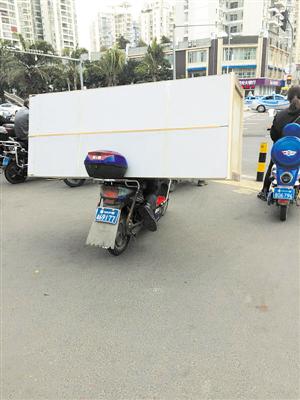 男子骑电动车载着一个近2米长的木柜在路上行驶。