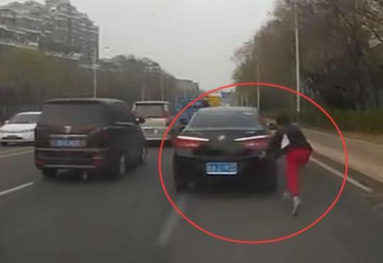 该女子为碰瓷在马路上追着车跑