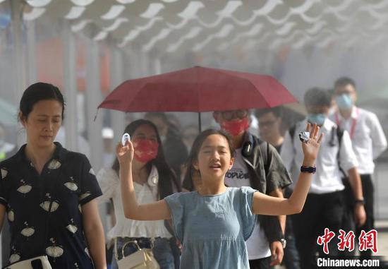 资料图:6月12日,重庆气温创新高 室外最高温超35℃,图为一小朋友经过广场上的水雾降温区域。 陈超 摄