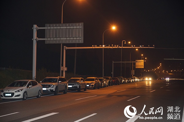 4月7日23时30分,武汉龚家岭收费站外,等待离汉的车辆排起长队。(张武军 摄)
