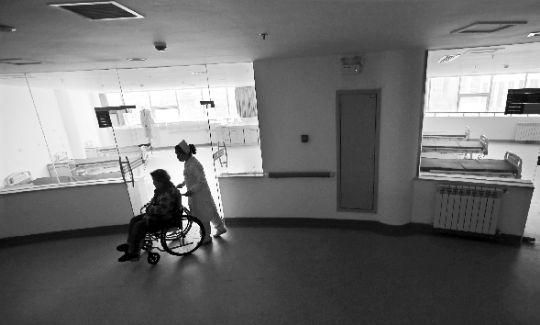 在湖北孝感市爱心护理院内，护士正推着一位轮椅上的老人走过空荡荡的楼道。本报记者 傅坚 摄