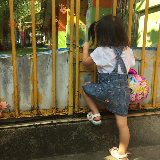8月17日，依依在家附近的小火车幼儿园偏门张望。   澎湃新闻记者 朱莹 实习生 张盼 图