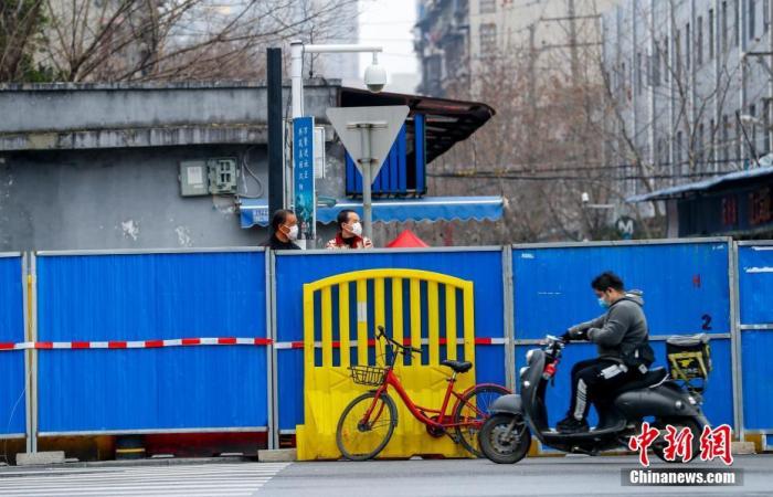3月6日，武汉汉阳鹦鹉大道，两位市民在墙内往外张望，一位市民骑车从墙外经过。 中新社记者 张畅 摄