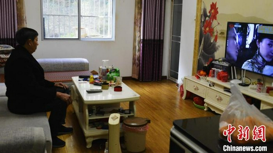 63岁的王胜斌在安置小区的家中看电视 乔长姣 摄