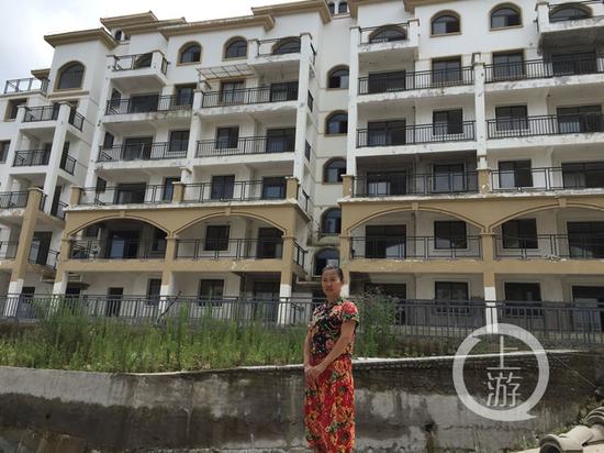 重庆购房者雷秀英站在独居的烂尾楼前合影，左上角晾晒有衣服的就是她居住的房间。