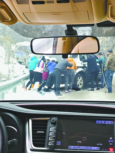 图为众人在冰雪中推出滑出道路的车辆    记者刘元聪 摄