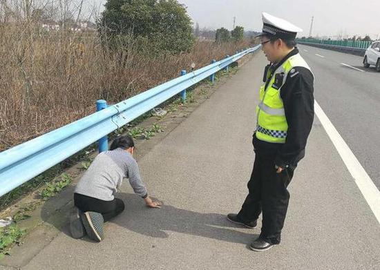 中年妇女双手撑在地面，双腿跪在高速上，跪拜着前进。