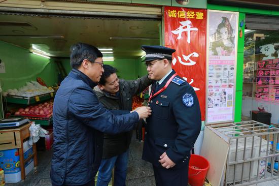 武汉市城管委主任张军与水果店店主王兆阳一起将“功勋城管”的荣誉勋章授予胡毅峰。