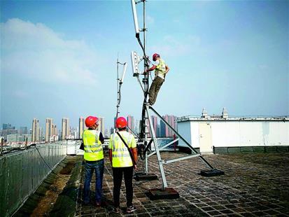 图为:上月,武汉移动公司工作人员在华中科技大学学生宿舍楼顶架设5G试验基站。