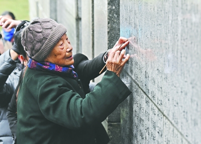 南京大屠杀幸存者夏淑琴给遇难者名单墙上亲人的名字添漆 新华社发