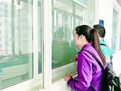 圖為：譚秋菊和丈夫隔著玻璃探視病床上的女兒