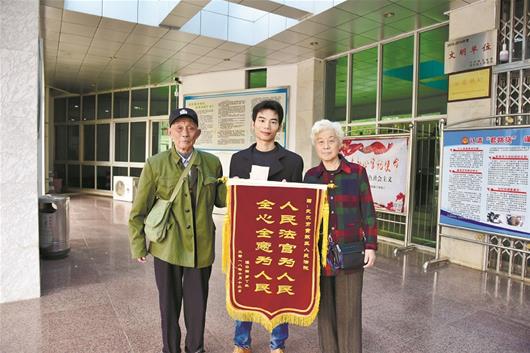 图为:91岁的罗爹爹(左)向法官送锦旗致谢