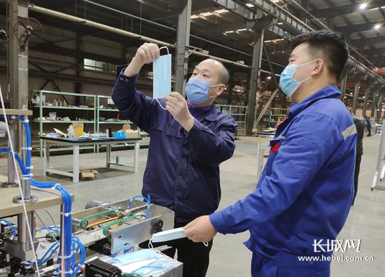 一线工人顾海亮（左）和高新乐正在分析新组装的口罩机生产的样品。记者袁立朋摄