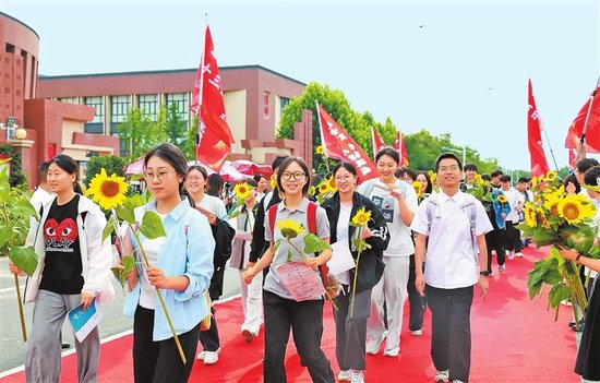 6月7日，在郑州国师实验高中，学生们手持向日葵出发前往考点。本报全媒体记者 张琮 摄
