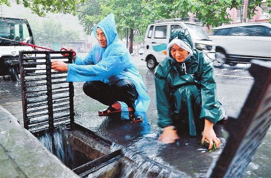 8月12日，许昌市魏都区城管局环卫所环卫工人在湖滨路捡拾道路排水口的树叶和垃圾，确保排水畅通。 牛书培 摄