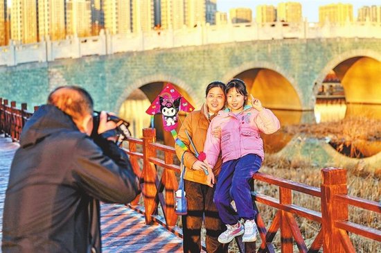 市民在郑州贾鲁河公园桥畔游玩拍照。