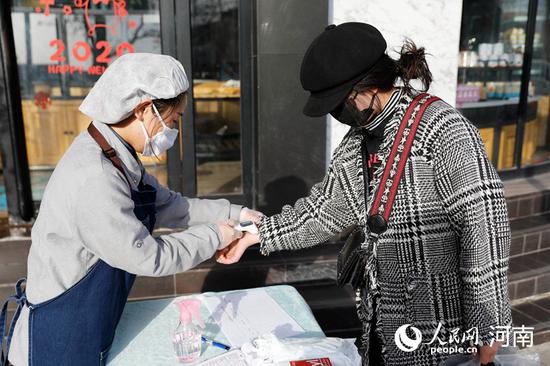 2月25日,河南省平顶山市宝丰县一家蛋糕店员工对顾客进行体温测量。何五昌 摄