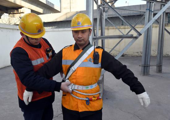 1月17日，在郑州东站附近的一座信号塔前，同事为牛军辉（右）检查安全带。