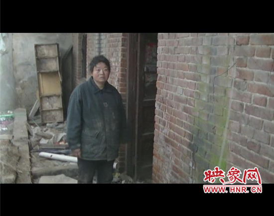 郝秋爽的母亲站在破旧的房子前。
