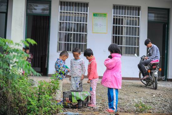 3月8日,课间休息时,孩子们在教室前的空地上玩耍,吴志平坐在摩托车上看手机。