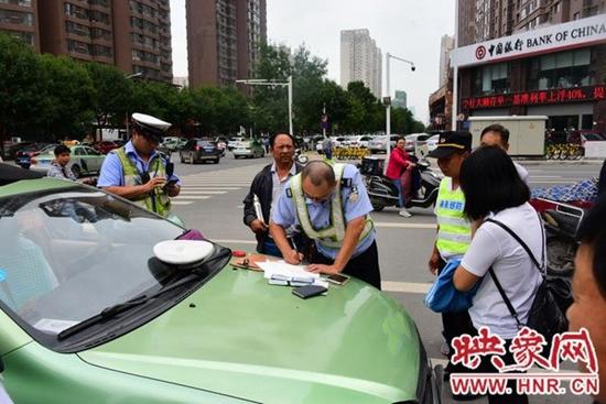 在路口的西南角，停着一辆出租车。郑州市交警四大队两名民警正向双方当事人询问情况。