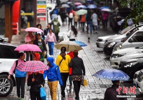 9月24日，新疆乌鲁木齐市降下秋雨，外出民众打着雨伞快步前行。 中新社记者 刘新 摄