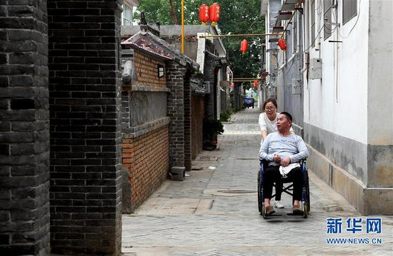 5月30日，韩红晓用轮椅推着丈夫贾洪涛外出活动。