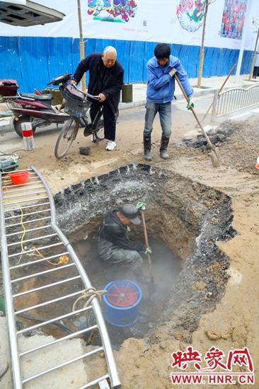 幾名熱力公司的工作人員正在開挖路面，現場流出的熱水被排到下水道中，熱氣騰騰。