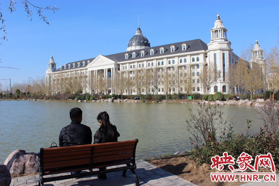 男女同学在湖边树下谈天说地，远处就是学校新建的西式教学楼。 